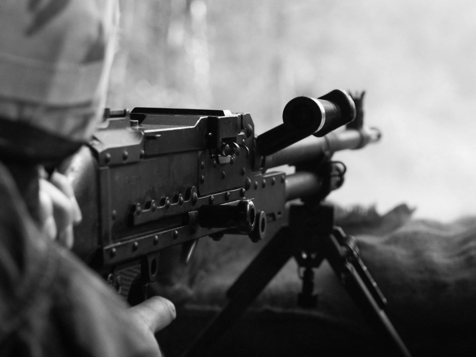 A close-up view of a man operating a machine gun, set against a blurred backdrop. This HD image serves as a striking desktop wallpaper and background.