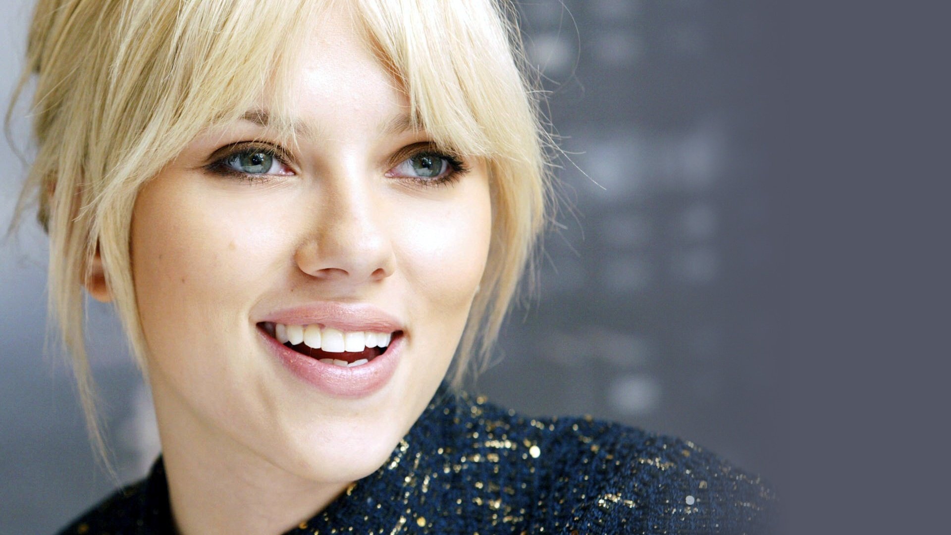 A close-up of Scarlett Johansson smiling, featuring her blonde hair and sparkling outfit, set against a blurred background. This HD image serves as a vibrant desktop wallpaper.