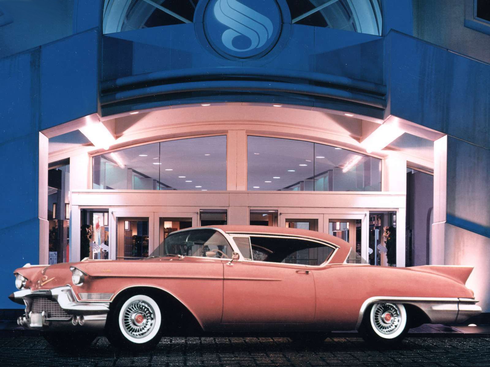 HD desktop wallpaper featuring a classic pink Cadillac parked in front of a modern building with large glass doors, showcasing vintage automotive elegance.