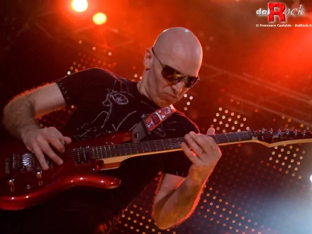 A dynamic HD desktop wallpaper featuring Joe Satriani passionately playing guitar under vibrant stage lights, capturing the essence of the music performance.