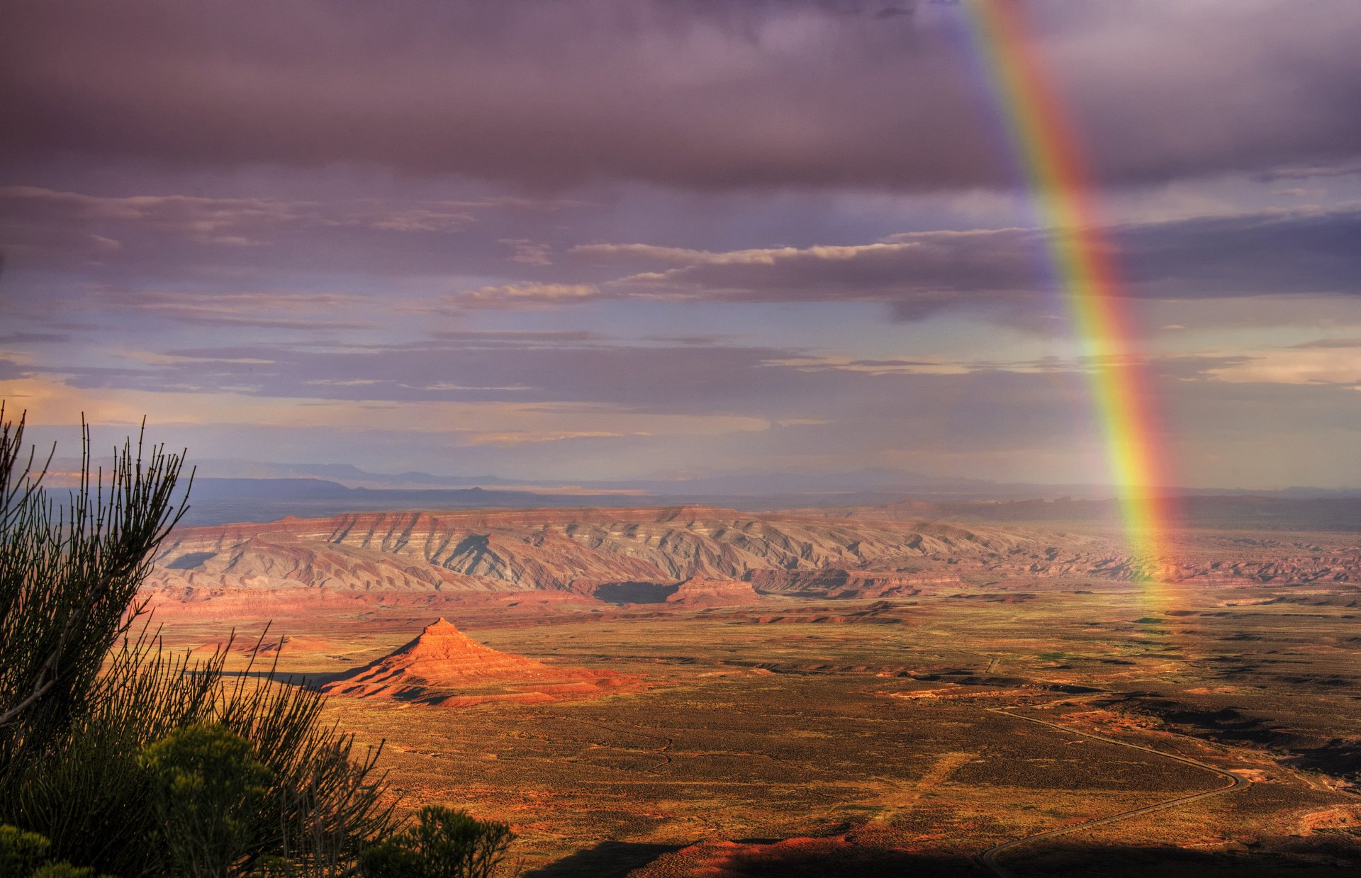 A vibrant rainbow arches over a vast desert landscape under a dramatic sky, captured in stunning 4K Ultra HD for a striking PC desktop wallpaper.