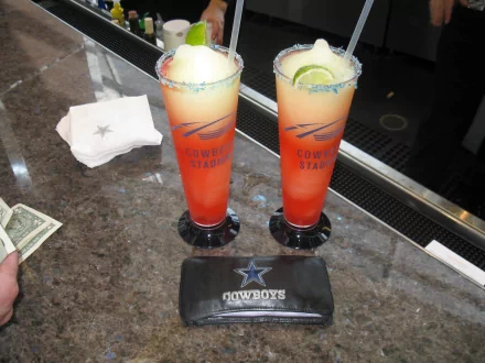 HD PC desktop wallpaper showing two colorful frozen cocktails with salted rims, a lime garnish, napkins, and a Cowboys branded wallet on a granite countertop.