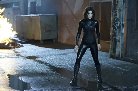 HD PC desktop wallpaper featuring a scene from the movie Underworld: Awakening, showing a character in a black combat suit standing in a dimly lit urban alley.