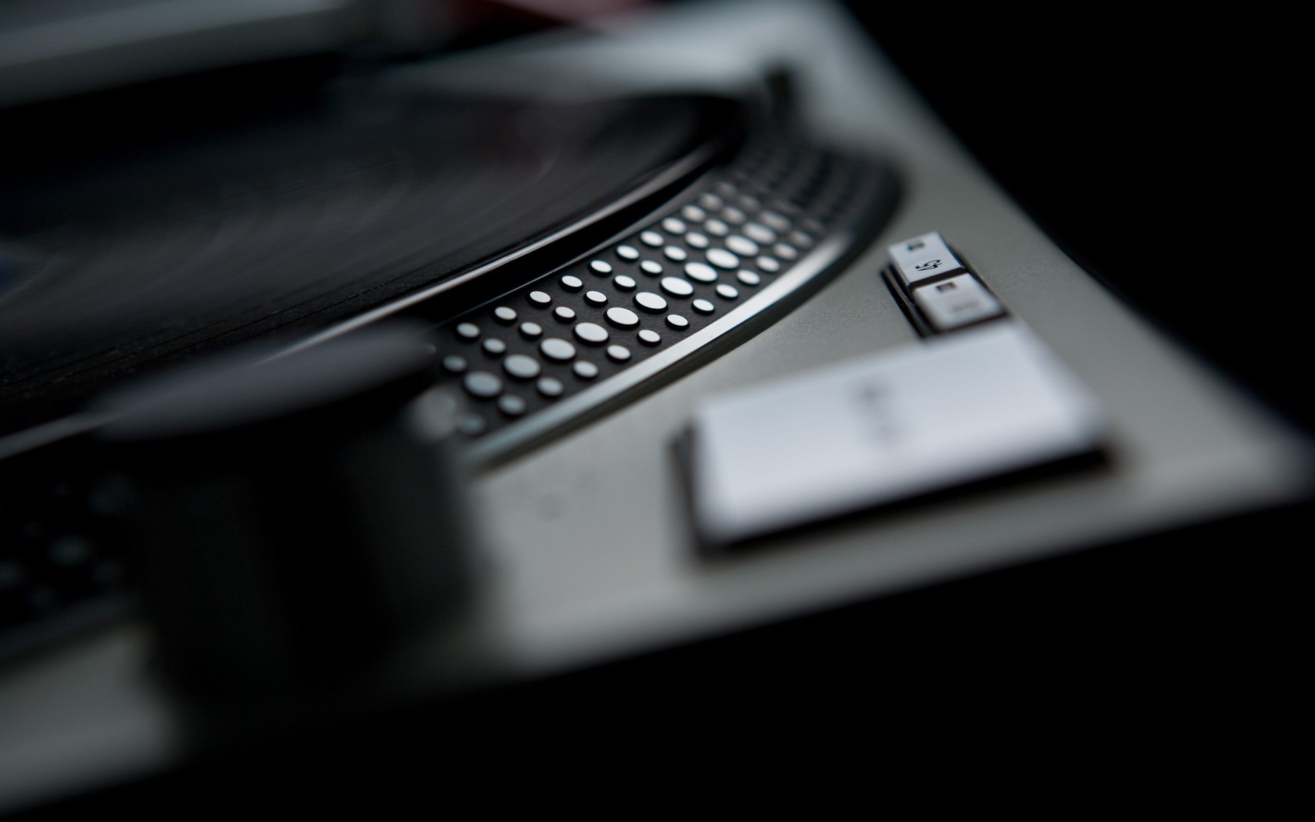 Close-up of a DJ turntable platter and controls in a dark studio; 2K Quad HD PC desktop wallpaper/background with a music studio vibe.