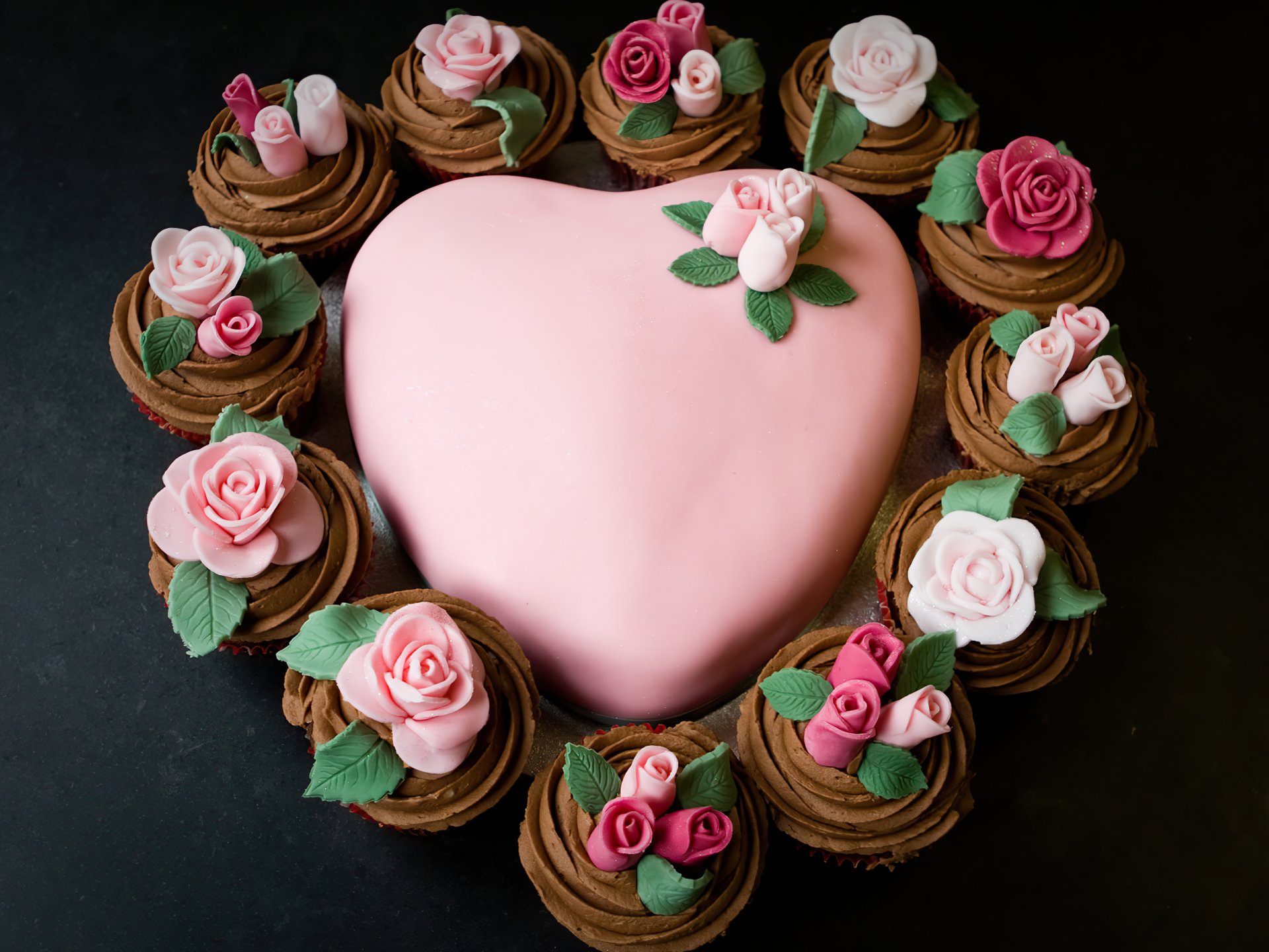 HD desktop wallpaper featuring a heart-shaped pink cake surrounded by chocolate cupcakes adorned with pink and white rose decorations.