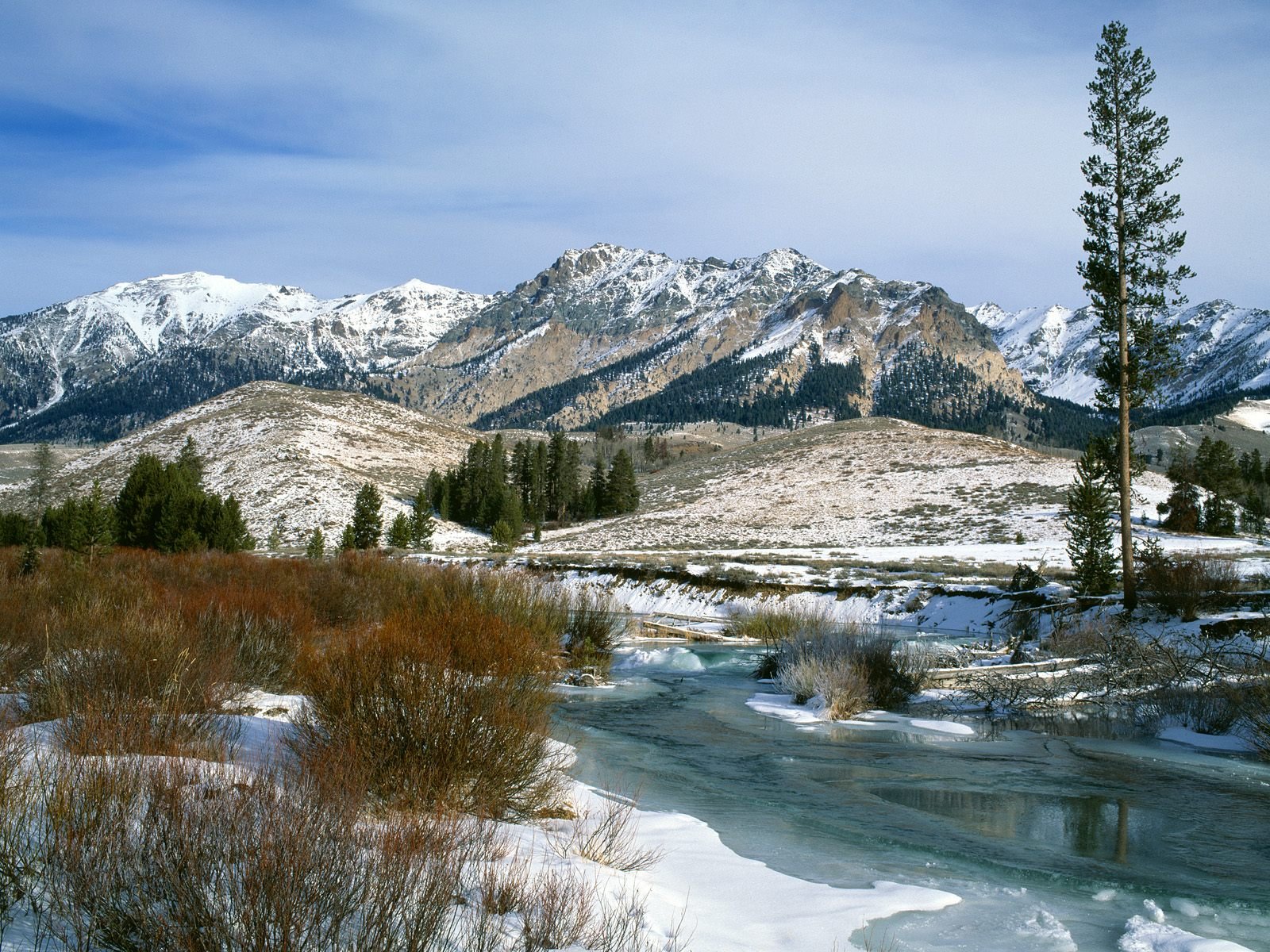 A serene winter landscape featuring snow-capped mountains, a winding icy river, and meadows, creating a stunning backdrop for a HD PC desktop wallpaper.