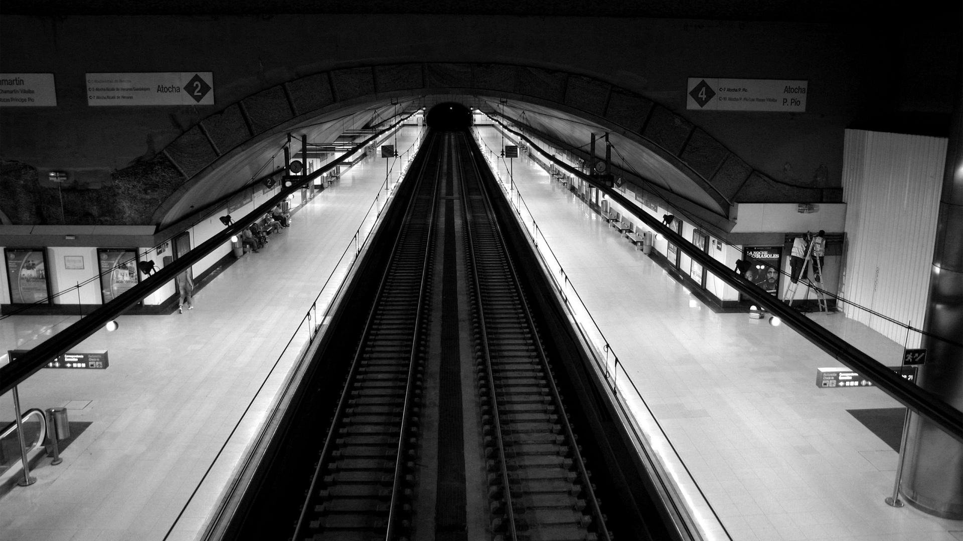 Black-and-white man-made subway interior with converging tracks and empty platforms, high-contrast composition — HD PC desktop wallpaper/background