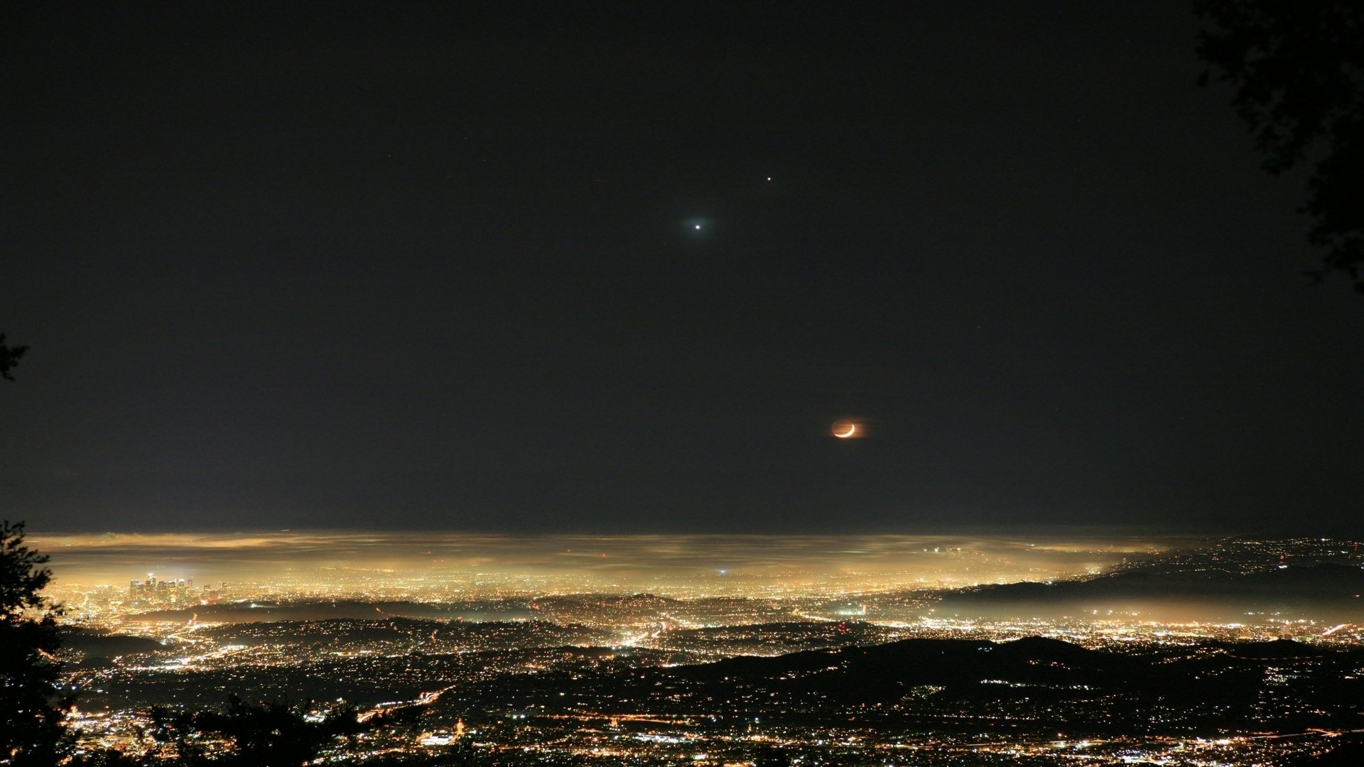 HD desktop wallpaper of a fog-covered cityscape at night, showcasing glowing lights and a scenic earth view under a dark sky.