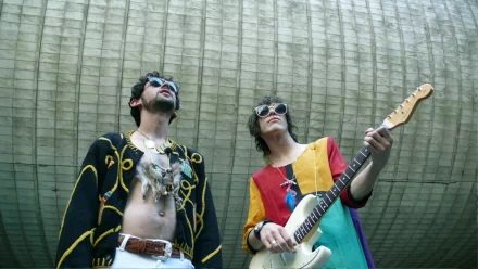 HD PC desktop wallpaper of two costumed musicians—one with an electric guitar—standing beneath a curved concrete canopy, conveying a psychedelic indie rock band vibe.