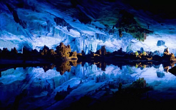 HD desktop wallpaper of the illuminated Reed Flute Cave showcasing vibrant blue and green stalactites reflected in still water inside a natural limestone cave.