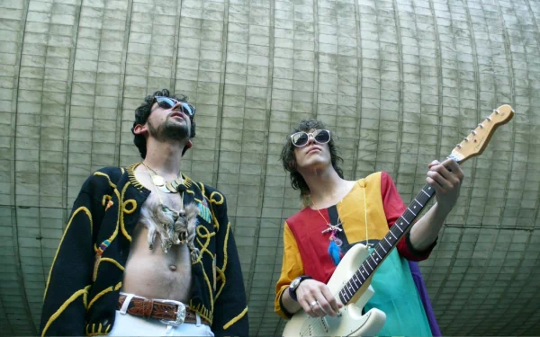 HD PC desktop wallpaper of two costumed musicians—one with an electric guitar—standing beneath a curved concrete canopy, conveying a psychedelic indie rock band vibe.