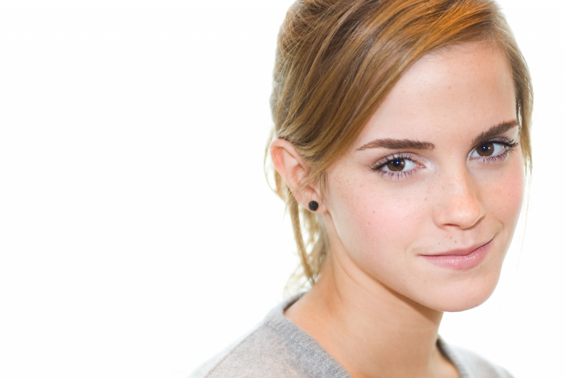 A high-definition desktop wallpaper featuring Emma Watson, showcasing her natural beauty with a soft focus on her expression against a light background.
