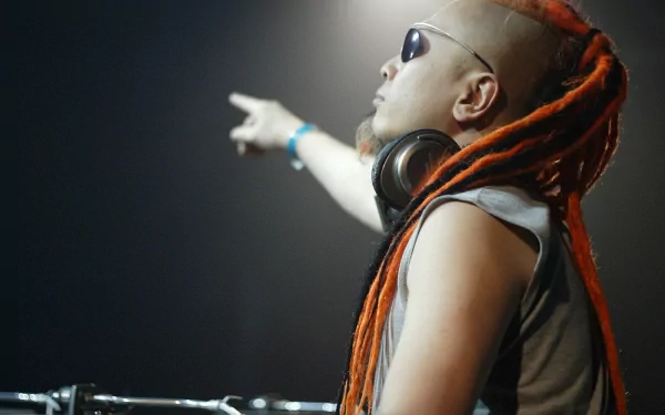 DJ with orange dreadlocks and sunglasses pointing into the distance while wearing headphones, set against a dark background. High-definition desktop wallpaper.