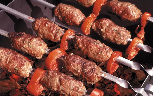 Close-up of skewers with seasoned meat and tomatoes grilling over charcoal, showcasing a delicious barbecue scene. This HD image serves as an enticing desktop wallpaper.