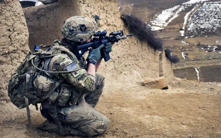 U.S. Army Infantry soldier in full combat gear firing a rifle in a mountainous warzone, captured in an HD military-themed desktop wallpaper.