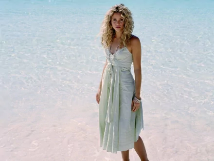 HD PC desktop wallpaper featuring Shakira standing in shallow, clear water, with a serene beach background highlighting her natural beauty and musical presence.