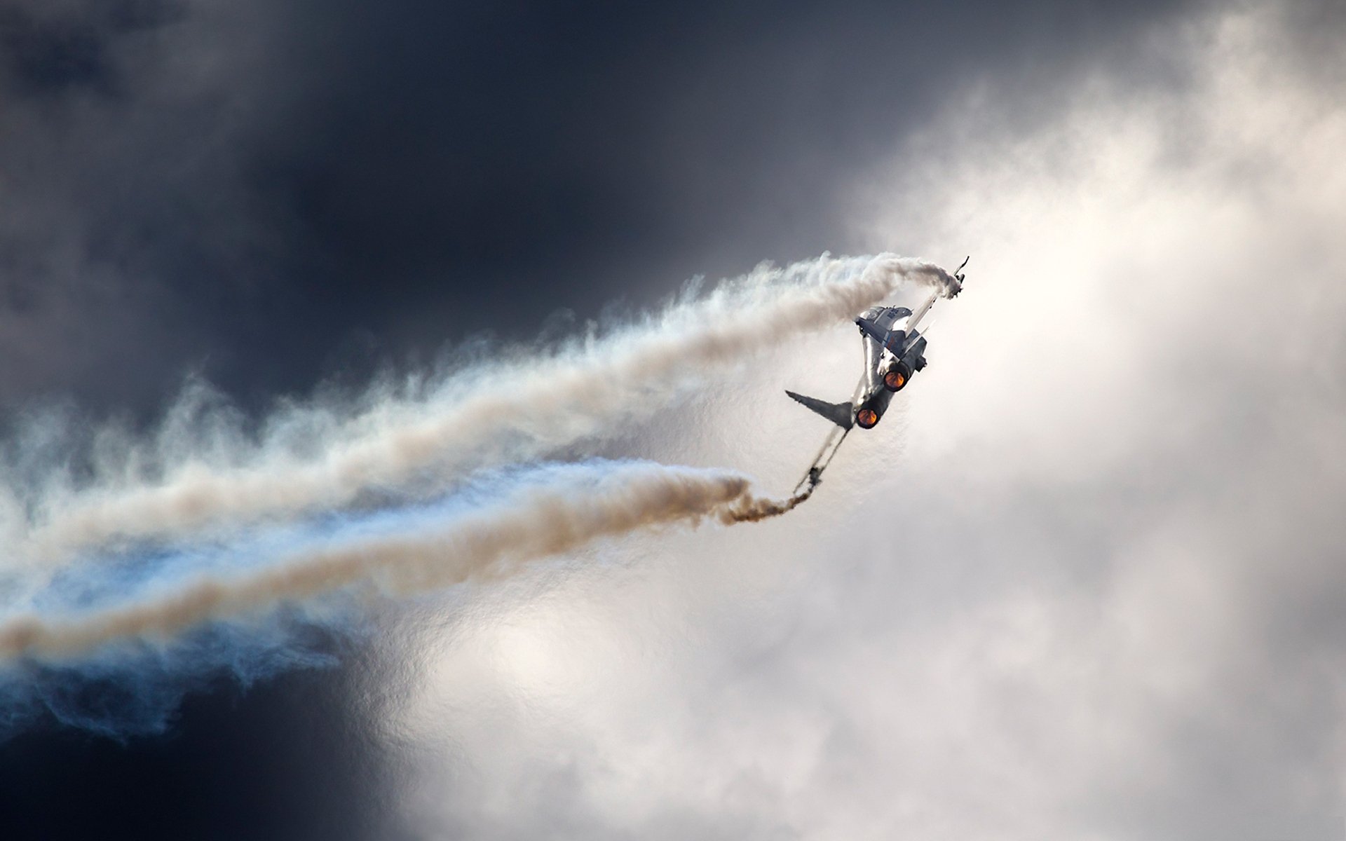 HD desktop wallpaper of a military aircraft performing an aerial maneuver, trailing smoke against a dramatic cloudy sky.