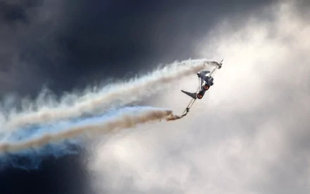 HD desktop wallpaper of a military aircraft performing an aerial maneuver, trailing smoke against a dramatic cloudy sky.