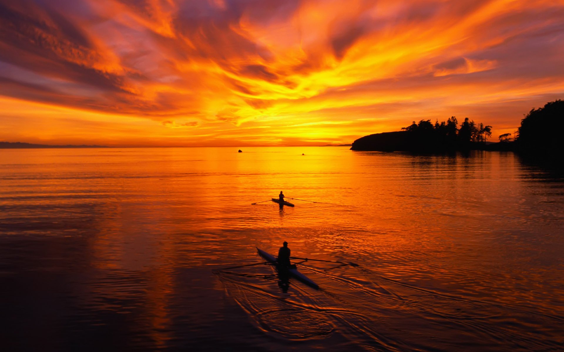 A breathtaking sunset paints the sky in vibrant oranges and purples, as two kayakers glide through calm waters, creating a serene and scenic backdrop for HD desktop wallpaper.
