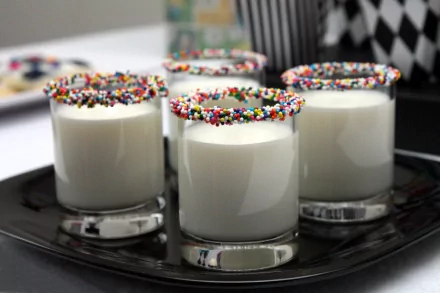 HD desktop wallpaper of four glasses filled with milk, each glass rimmed with colorful sprinkles, set on a sleek black tray.