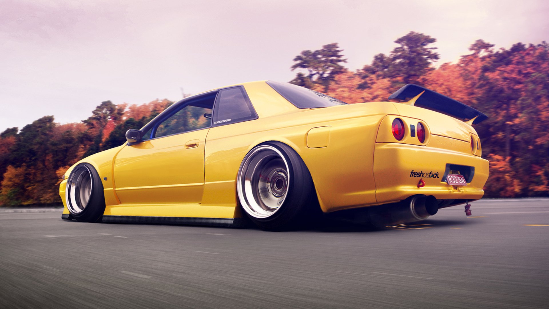 HD PC desktop wallpaper featuring a lowered yellow Nissan sports car driving on a road with blurred trees in the background.