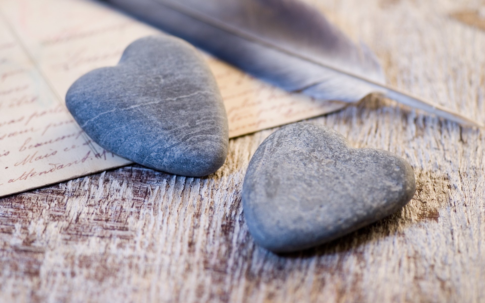 Artistic HD PC desktop wallpaper featuring two heart-shaped stones resting on a rustic wooden surface with a feather and handwritten letters, evoking love and nostalgia.