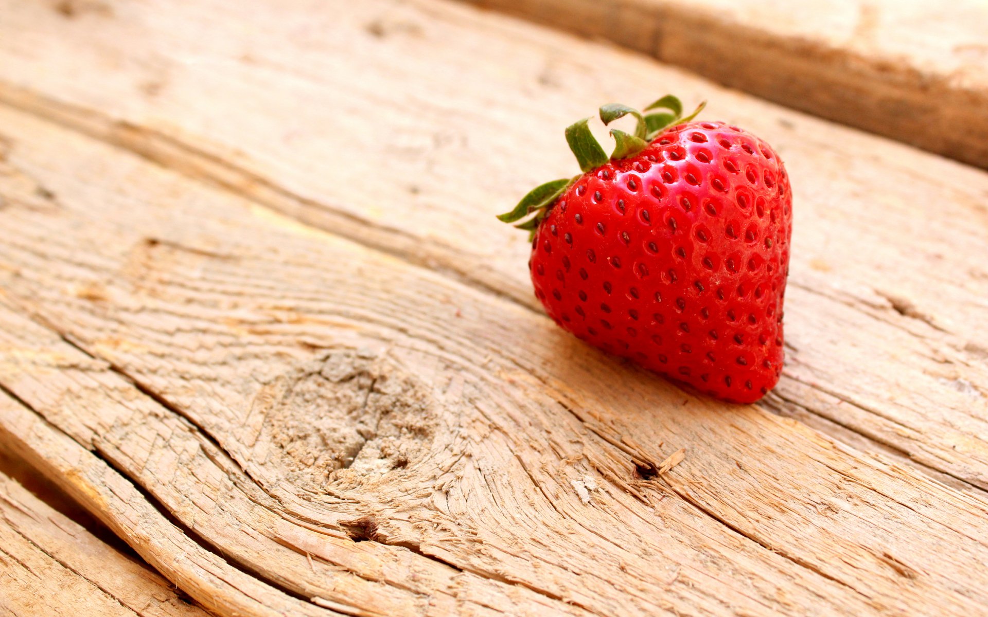 HD PC desktop wallpaper featuring a vibrant red strawberry resting on textured wooden planks, highlighting fresh food in a natural setting.