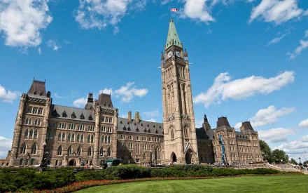 HD PC desktop wallpaper of man-made Gothic Revival architecture: a grand parliamentary building with central clock tower, blue sky and manicured lawn.