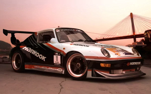 HD desktop wallpaper featuring a sleek sports car with racing decals, set against a sunset backdrop near a suspension bridge.