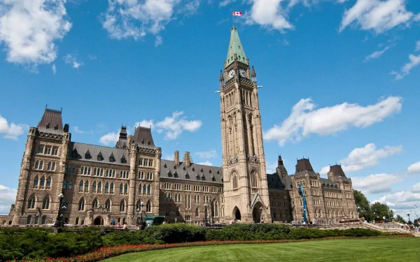 HD PC desktop wallpaper of man-made Gothic Revival architecture: a grand parliamentary building with central clock tower, blue sky and manicured lawn.