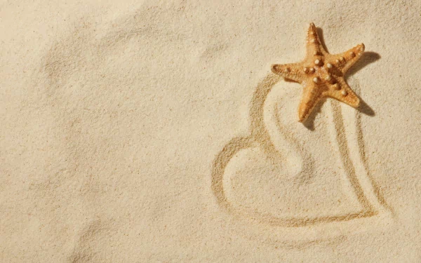 A starfish rests on smooth beach sand beside an artistic heart shape drawn in the sand, captured in HD for a serene desktop wallpaper.
