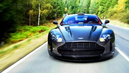 HD PC desktop wallpaper featuring a sleek black Aston Martin DBS driving on a forest-lined road.