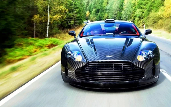 HD PC desktop wallpaper featuring a sleek black Aston Martin DBS driving on a forest-lined road.