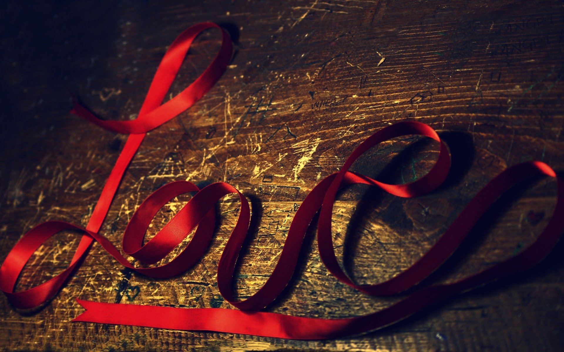 Artistic HD desktop wallpaper featuring the word Love crafted from a flowing red ribbon against a textured wooden background, evoking warmth and affection.