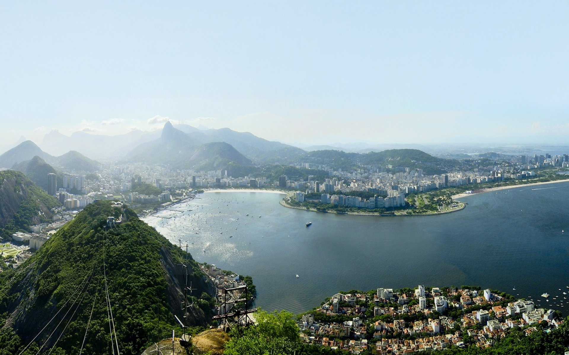 Panoramic HD wallpaper of Rio de Janeiro, Brazil, showcasing the cityscape, coastline, and green hills under a clear sky.