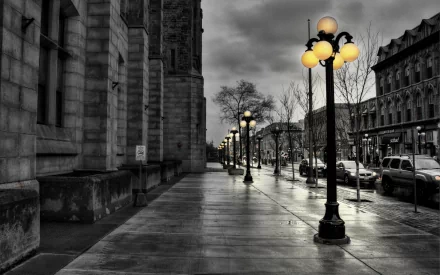 HD PC desktop wallpaper showing a moody city street scene with glowing street lamps, wet pavement, and historic man-made architecture under a cloudy sky.