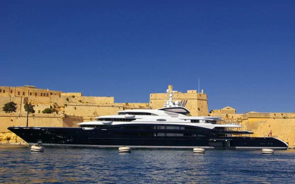 HD desktop wallpaper featuring a sleek black and white yacht docked near historic stone fortifications under a clear blue sky.