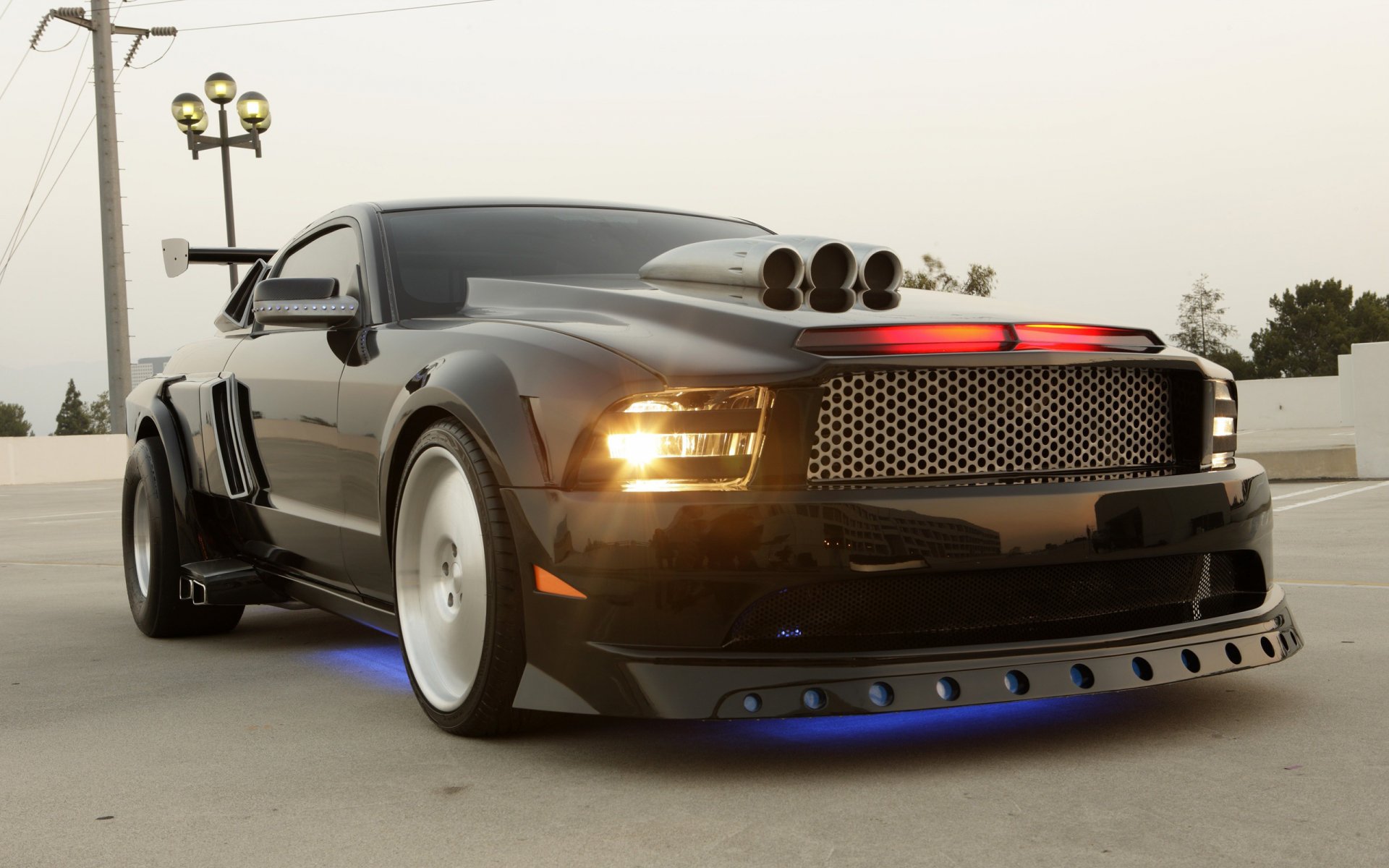 HD desktop wallpaper of a modified Ford Mustang, showcasing its sleek, powerful design with custom bodywork, prominent grill, and unique lighting in a street setting.