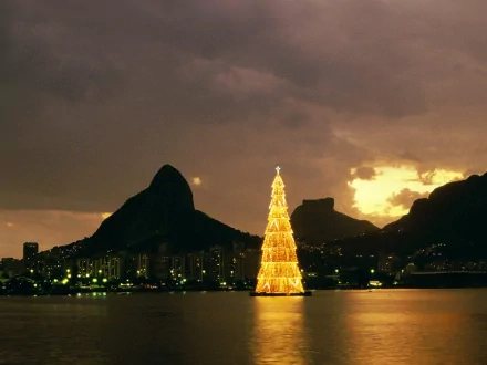 HD wallpaper of a glowing Christmas tree set against Rio de Janeiro's cityscape at dusk, with mountains in the background. Tags: Brazil, Rio de Janeiro, Christmas tree, holiday, Christmas.