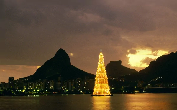HD wallpaper of a glowing Christmas tree set against Rio de Janeiro's cityscape at dusk, with mountains in the background. Tags: Brazil, Rio de Janeiro, Christmas tree, holiday, Christmas.