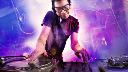 A vibrant HD desktop wallpaper featuring a DJ energetically mixing on turntables, surrounded by colorful lights and effects, capturing the essence of music and nightlife.