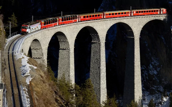 HD PC desktop wallpaper background: RhB red train (vehicle) curves across a stone viaduct above a snowy Swiss gorge.