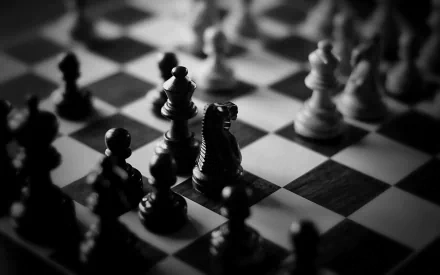 Black and white HD desktop wallpaper featuring a strategic chess game in progress, highlighting the intricate man-made design of the chess pieces on the board.
