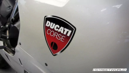 Close-up of a white Ducati motorcycle fairing featuring a red Ducati Corse badge — HD PC desktop wallpaper and background.