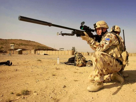 A soldier in camouflage crouches with a sniper rifle, poised for action in a desert landscape, showcasing military precision and focus. HD wallpaper setting.