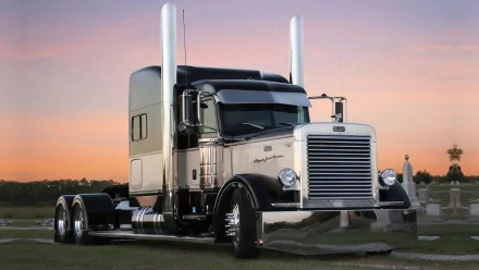 HD desktop wallpaper featuring a sleek Peterbilt vehicle parked on a grassy field at sunset with a soft pink and orange sky.