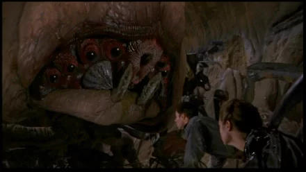 HD PC desktop wallpaper from the movie Starship Troopers: soldiers crouch in a cavern, recoiling from a giant alien bug's gaping maw and rows of teeth.