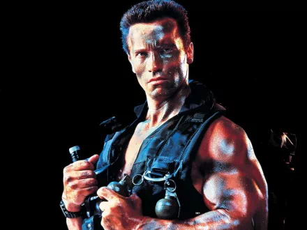 Arnold Schwarzenegger, in a striking pose from the movie Predator, showcases his muscular physique against a dark backdrop in this HD desktop wallpaper.