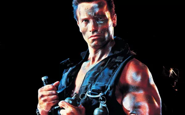 Arnold Schwarzenegger, in a striking pose from the movie Predator, showcases his muscular physique against a dark backdrop in this HD desktop wallpaper.