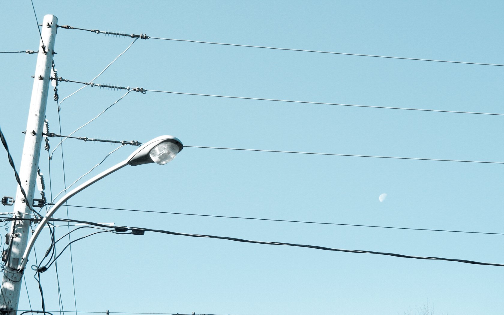 HD PC desktop wallpaper showing man-made power lines and a streetlight crossing a pale blue sky with a small crescent moon.